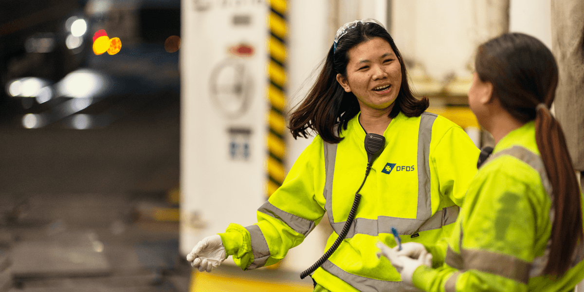 Two female DFDS seafarers on a vessel, wearing yellow security clothing, talking to each other