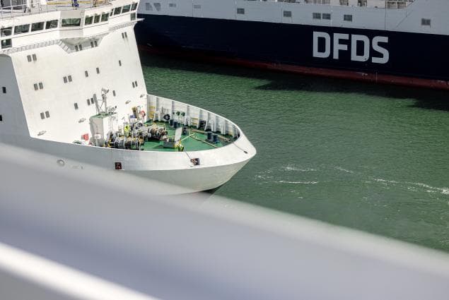 A white ship seen in the harbour, with in the background a DFDS vessel, with dark-blue colouring