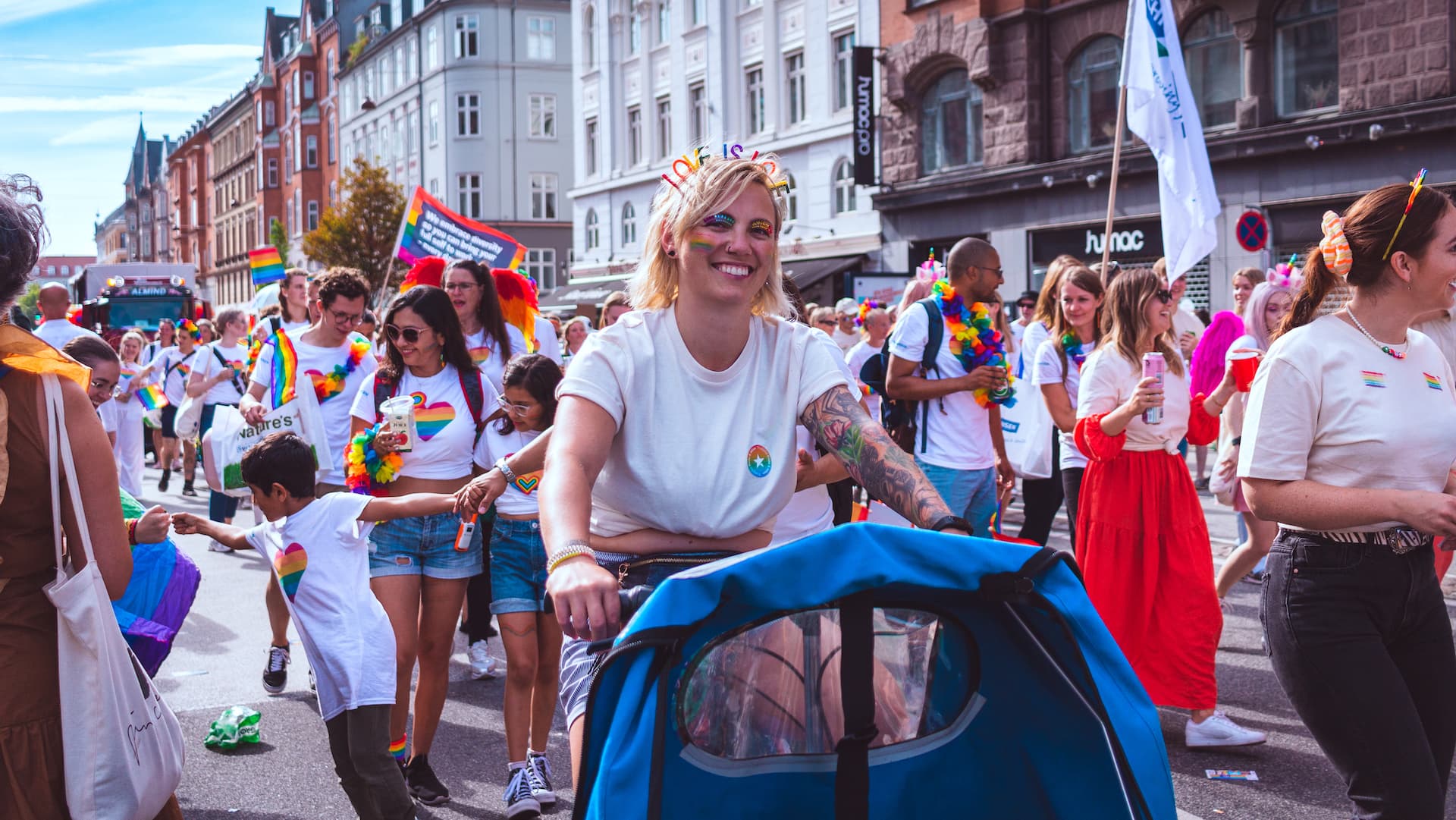Parade of cheering crowd in public space, with clothed in white t-shirts with rainbow colours, flags and banners - copyright ph. Rikke Høyen