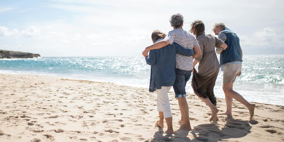 Friends walking arm in arm along the white sand beach