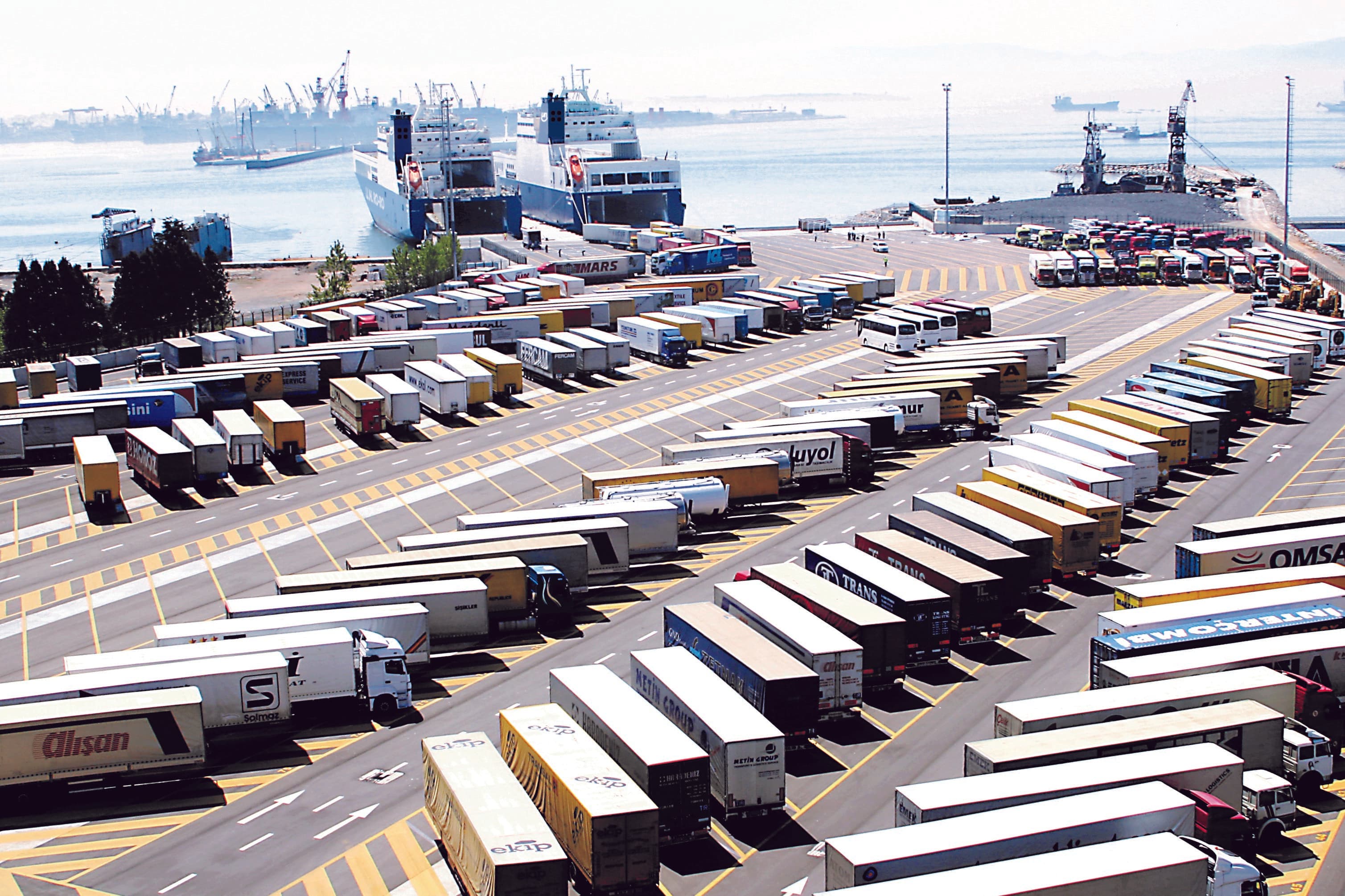 Trucks and lorries parked at a port in Pendik, with two vessels docked in the background