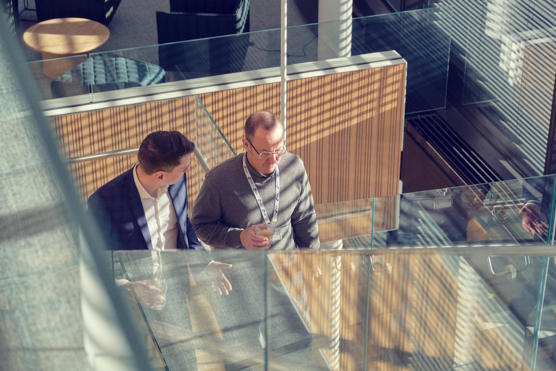Two employees on stairway in DFDS Office, climbing up, both with a cup of coffee in hand