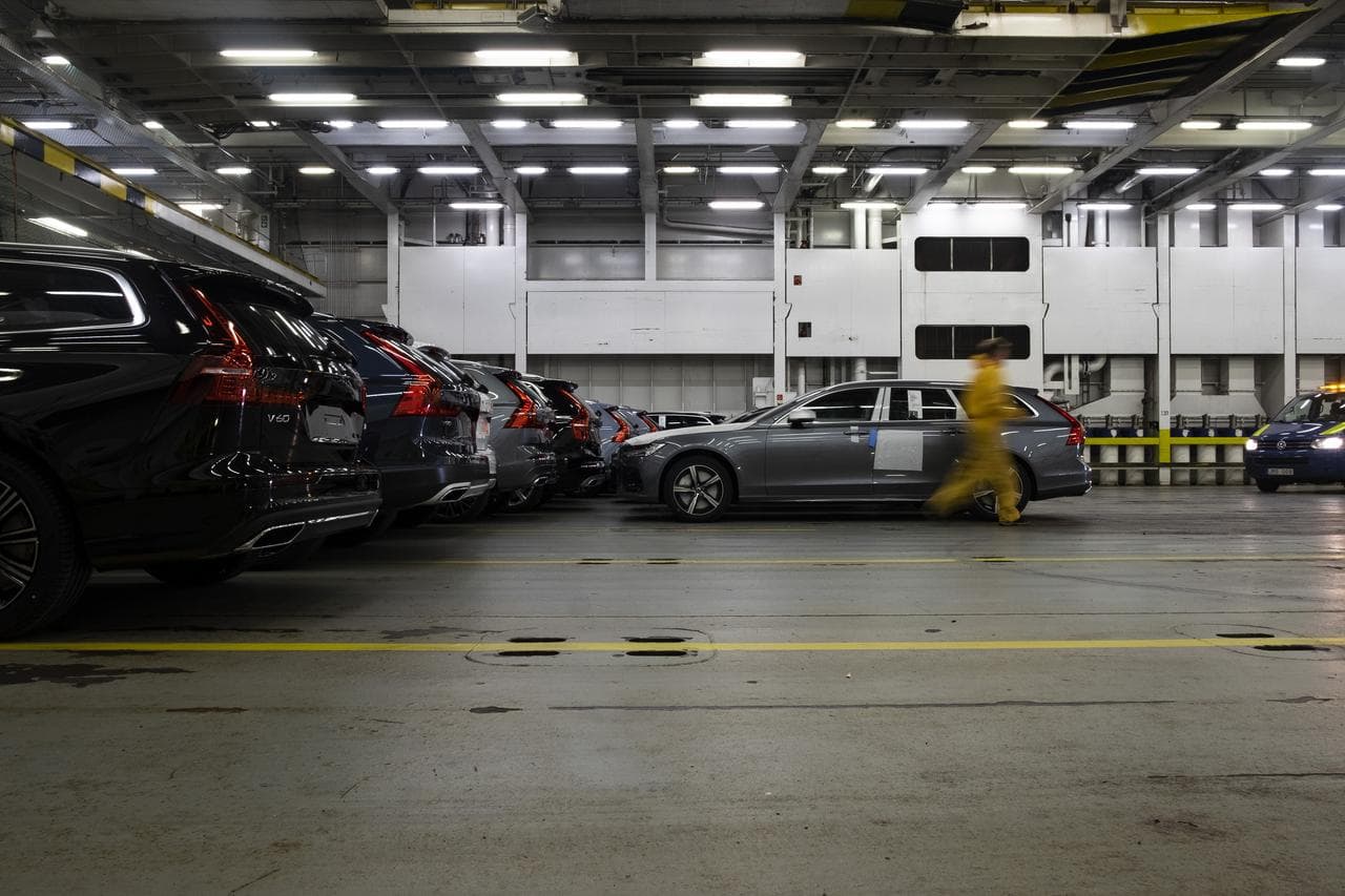 New cars loaded on a ship deck, with a man in yellow working clothes walking away from it