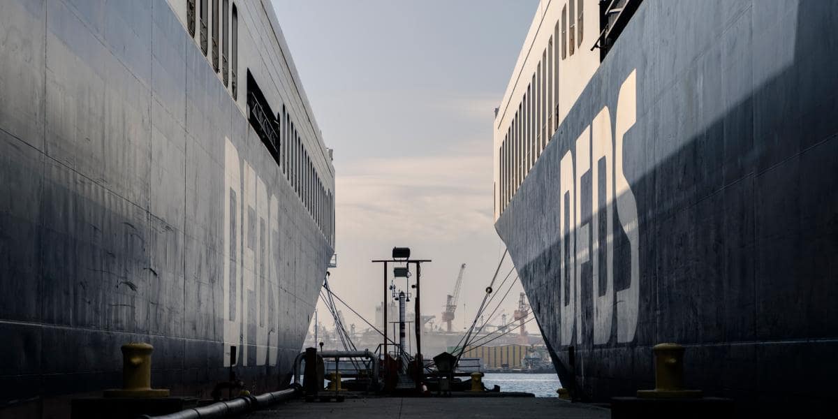 Two DFDS vessels are lying opposite each other on the quay, with on the horizon the sight of the harbour with cranes, other vessels, and warehouses