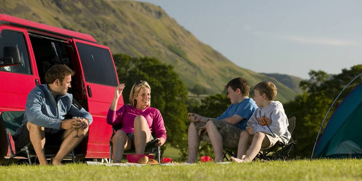 Family sitting outside car with tent